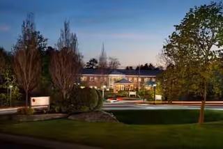 Exterior view of The Cedars senior living facility at dusk with landscaped grounds and entrance.