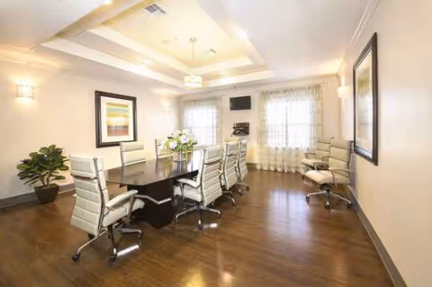 Bright interior meeting room with a long dark table, cream chairs, and windows.
