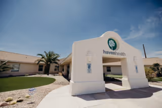 Entrance archway of Haven Health Lake Havasu facility with a clear blue sky, a palm tree, and a single-story building in the background.