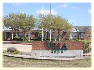 Exterior view of Villa South Assisted Living and Memory Care facility showing a brick sign with the name 'Villa' and the number '4834' in front of a building with trees and a clear sky.