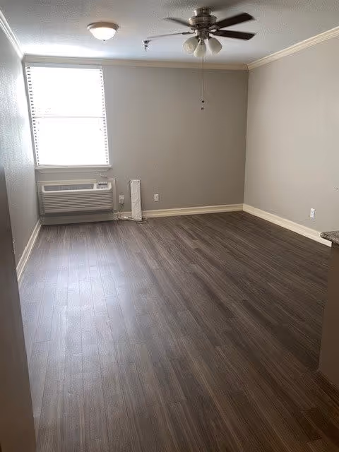 Empty room with dark wood-look flooring, gray walls, a ceiling fan, and a window air-conditioning unit.