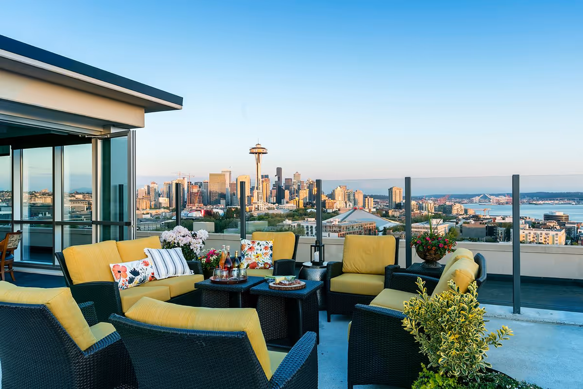 Rooftop terrace with wicker seating and yellow cushions overlooking the Seattle skyline, including the Space Needle.