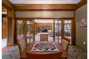 Interior view of a common area in a senior living facility featuring a table with a checkers board and pieces in the foreground. The room has wooden trim, glass-paneled doors, and comfortable seating visible in the background.