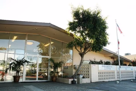 Paramount Convalescent Hospital exterior with glass doors, trees, and an American flag.