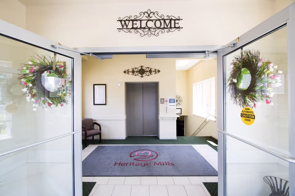 View of the entrance lobby at Heritage Mills, featuring a welcome sign, decorative wreaths, and an elevator door.