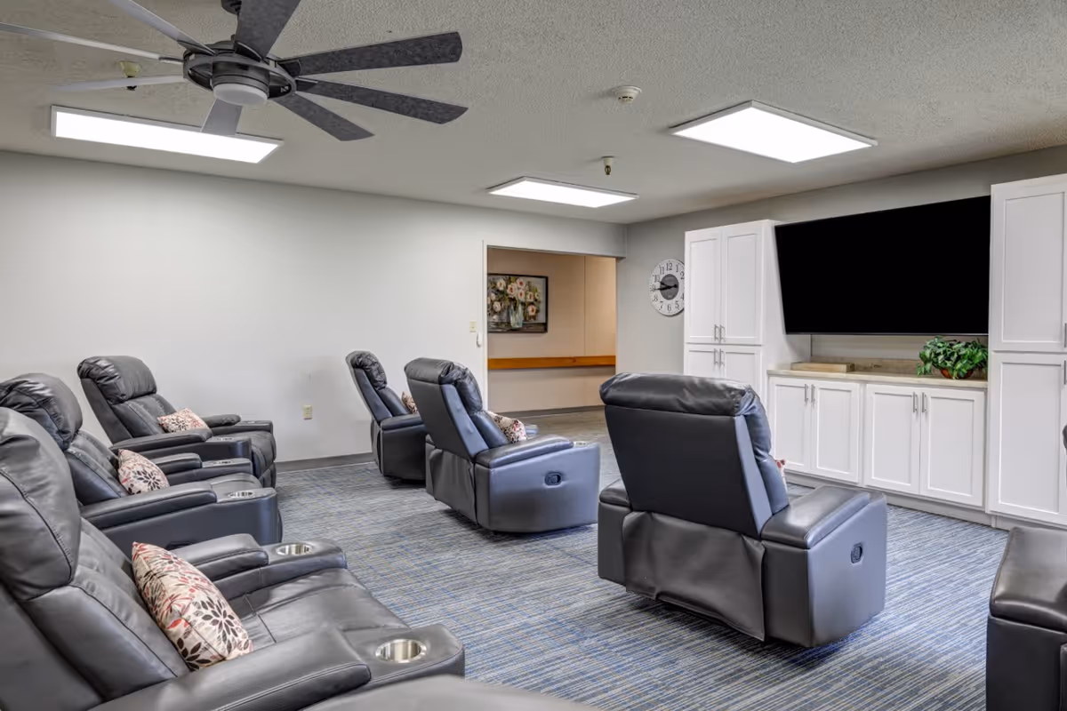 A common lounge with multiple leather recliners arranged facing a large wall-mounted TV and white cabinets.