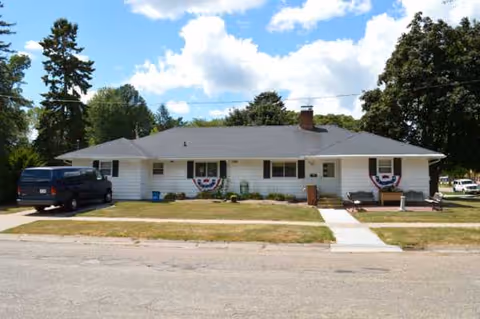 White, single-story Casa De Oakes Baraboo facility with walkway and parked van.