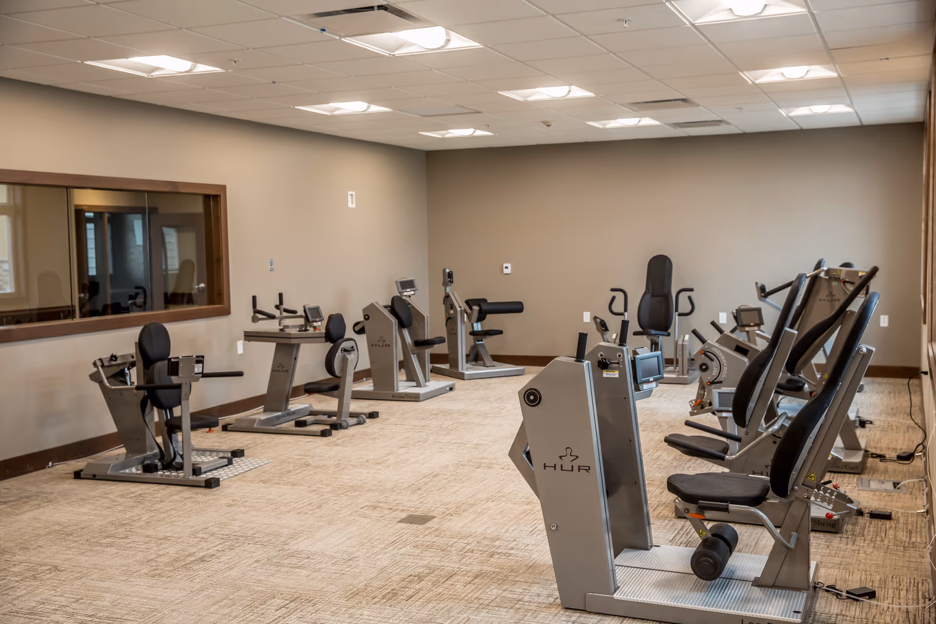 Well-lit exercise room with several seated strength-training machines arranged on a carpeted floor.