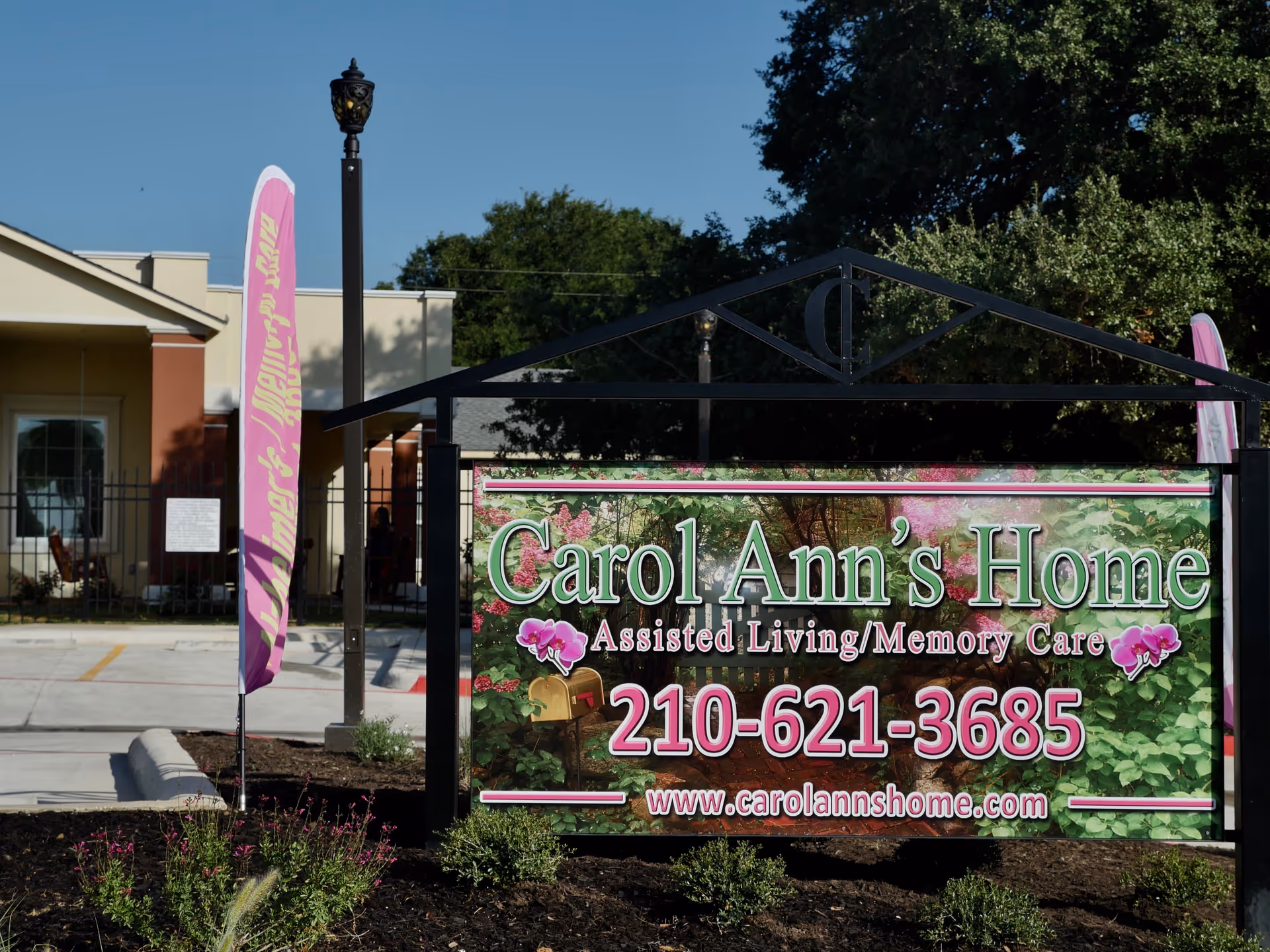 A large outdoor sign for Carol Ann's Home Assisted Living/Memory Care with phone number and website in front of the facility entrance.
