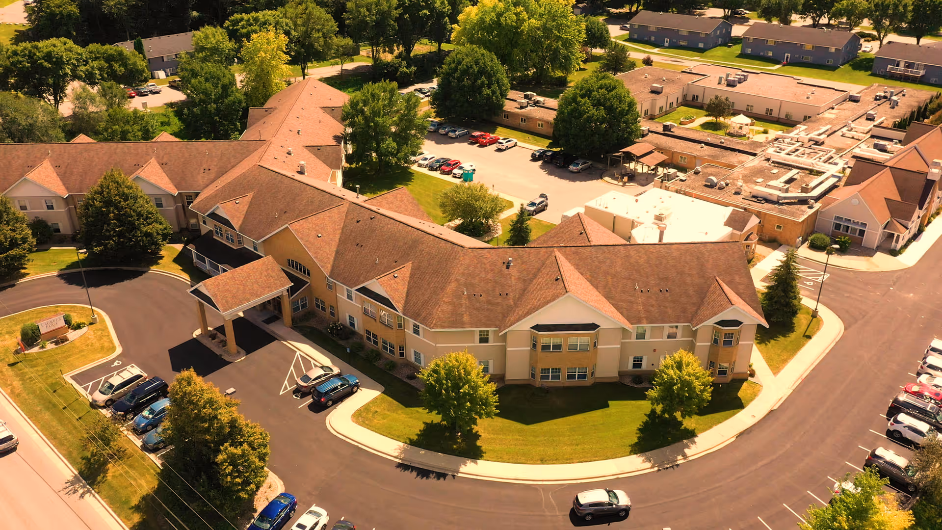 Aerial view of Laurels Peak Rehabilitation Center showing a large L-shaped beige building with parking lots, driveways, and surrounding trees.