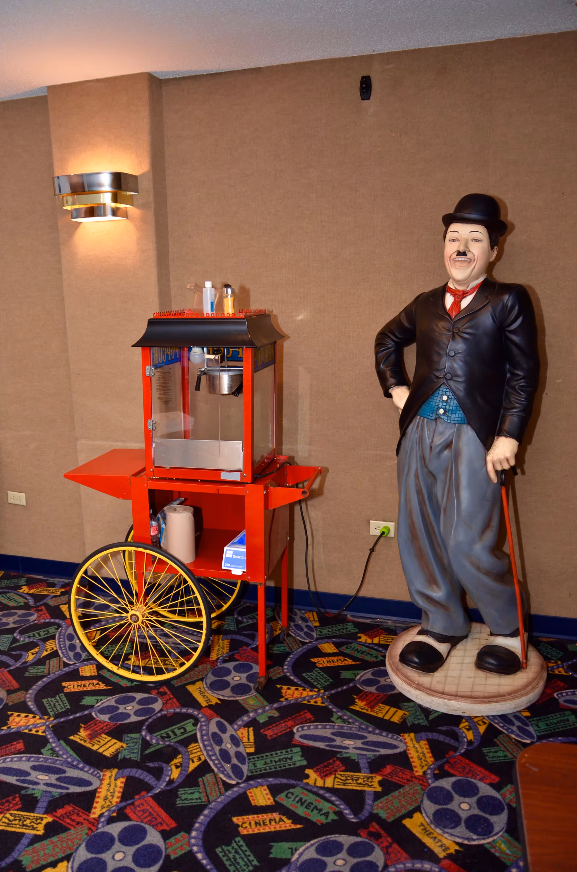 A cinema-themed interior corner with a red popcorn cart and a life-size statue of a man wearing a bowler hat and holding a cane.
