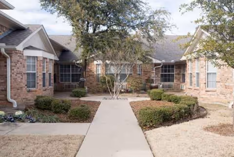 Brick senior living facility exterior with a central walkway and manicured shrubs.