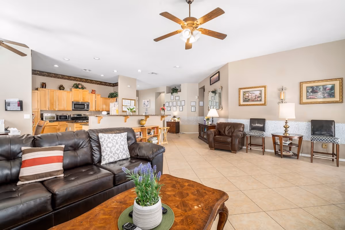 Bright communal living room with leather sofas, armchairs, a coffee table and an open kitchen visible in the background.