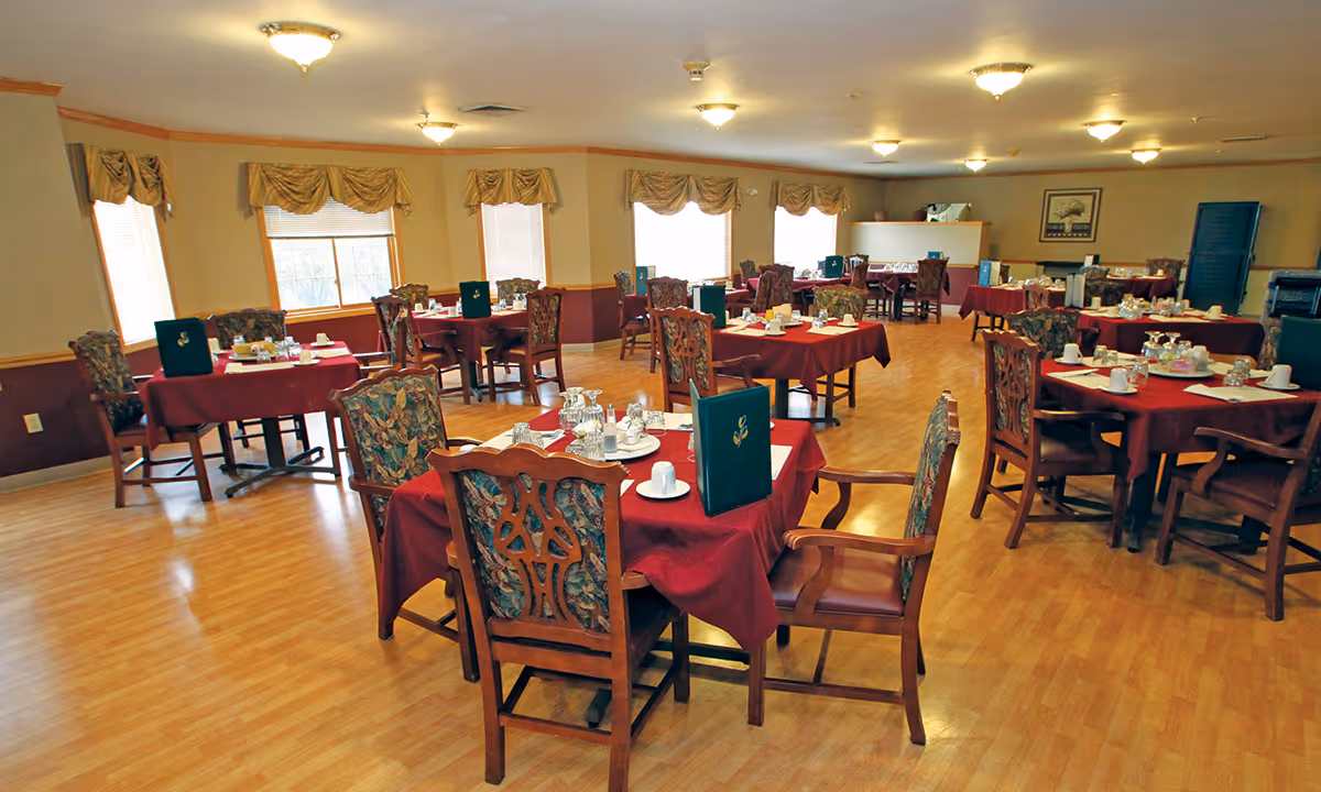 Dining room with multiple tables set with red tablecloths and place settings in a senior living facility.