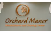 Wall sign displaying the name 'Orchard Manor Rehabilitation and Nursing Center' with a circular logo featuring a tree above the text.