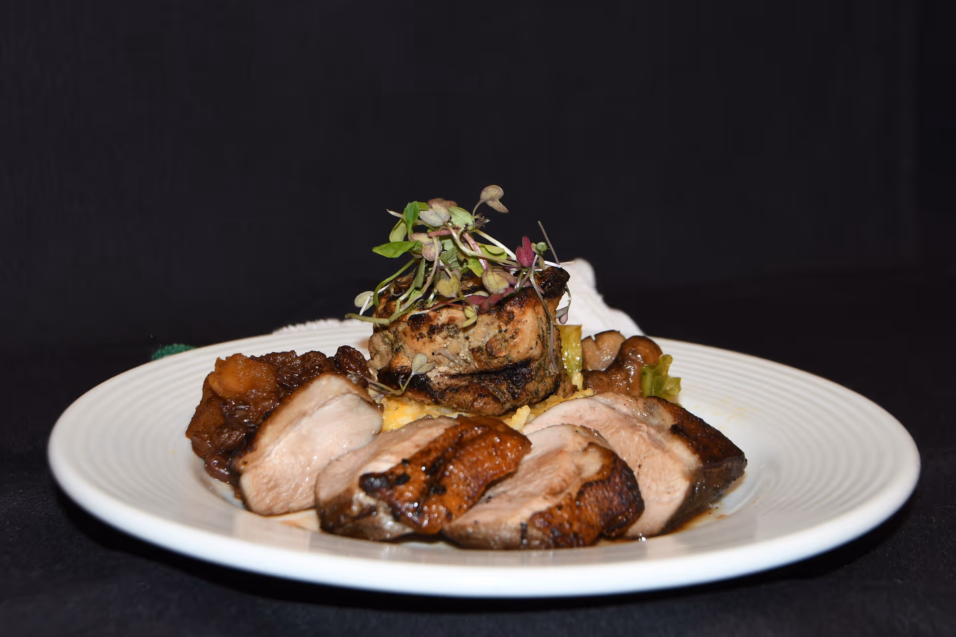 Plated slices of cooked meat garnished with microgreens on a white plate against a dark background.