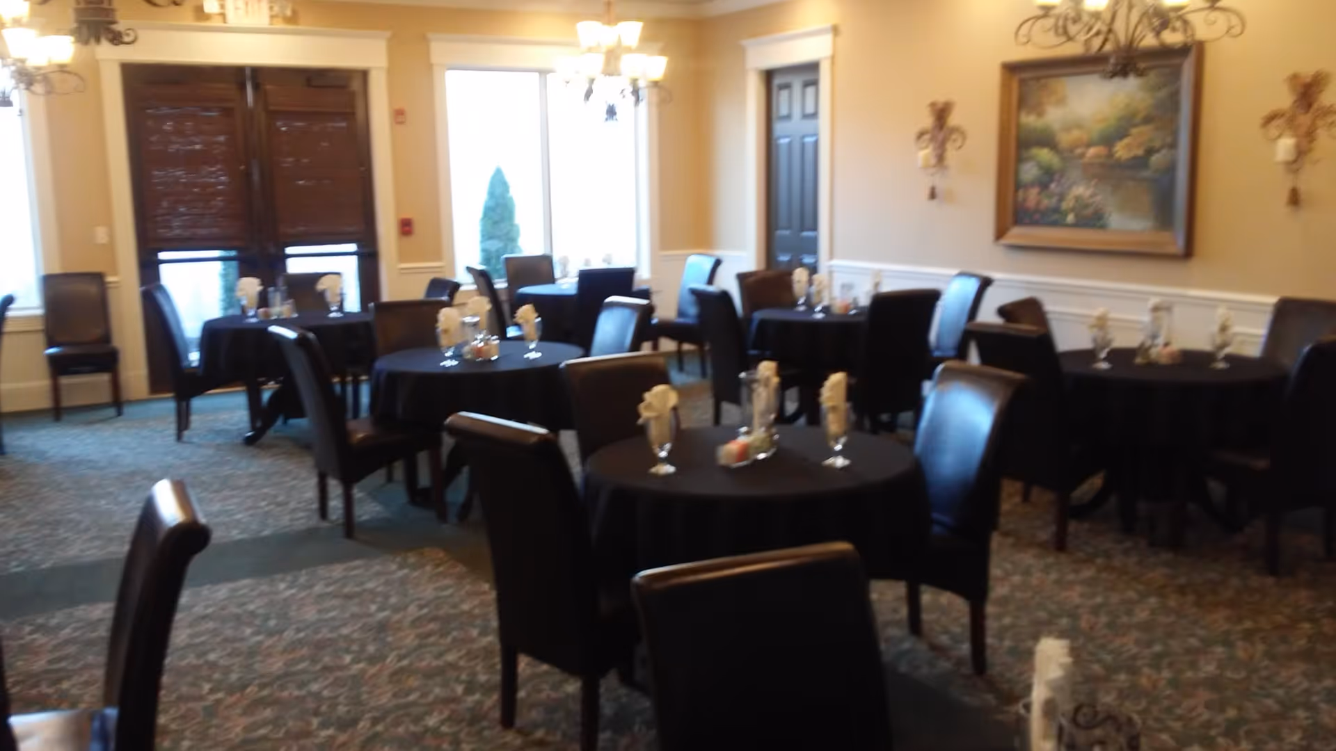 Dining room with round tables covered in dark tablecloths and leather chairs, set with napkins and glassware.