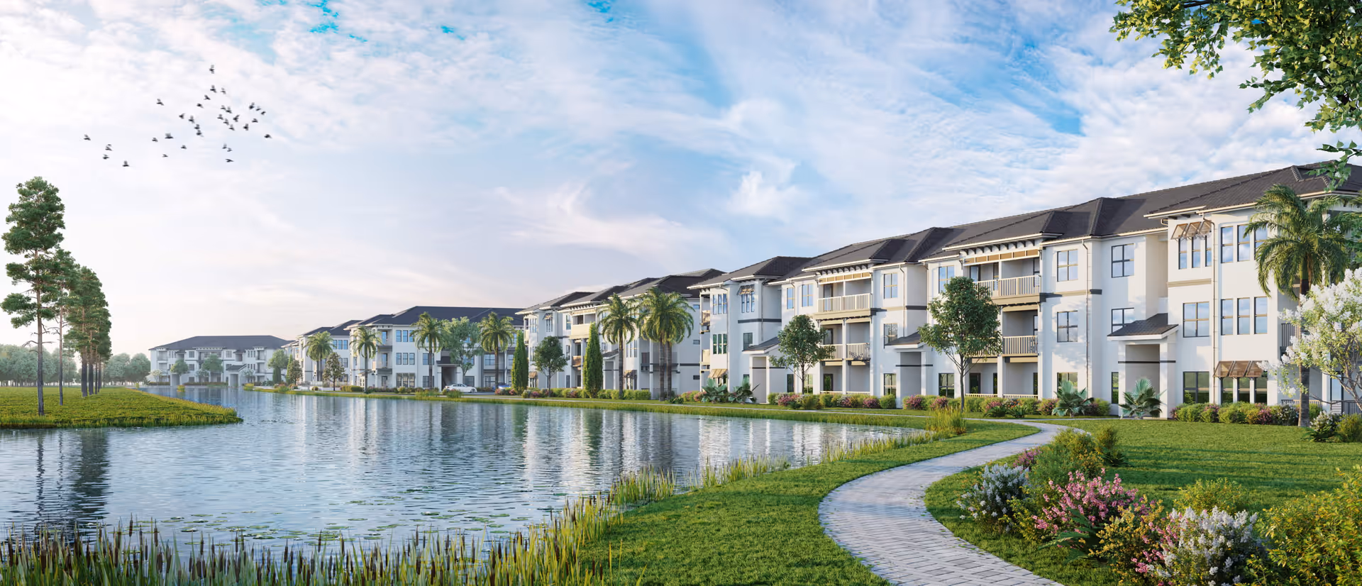 Panoramic exterior view of multi-story residential buildings lining a landscaped lakeside walkway with palm trees and a pond.