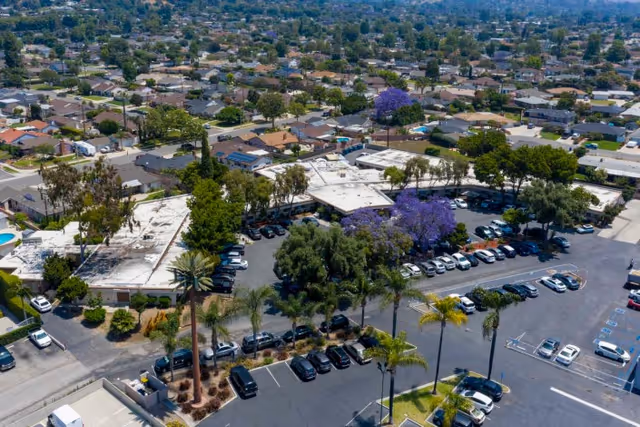 Aerial view of the Whittier Hills Healthcare Center single-story building complex with parked cars, purple-flowering trees, and surrounding residential neighborhood.
