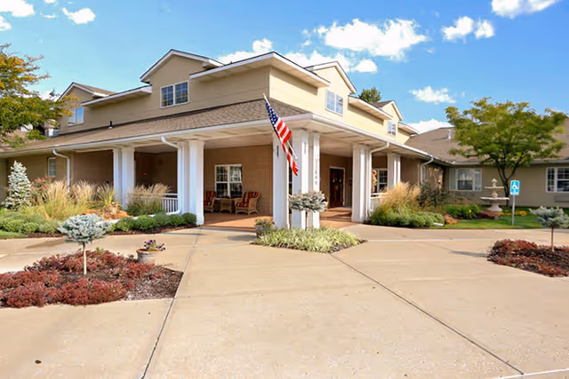 Brookdale Shawnee exterior with entrance, columns, flag, and landscaped front walkway