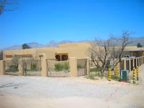 Tan desert-style senior care home exterior with metal fence, gate, and mountain backdrop.