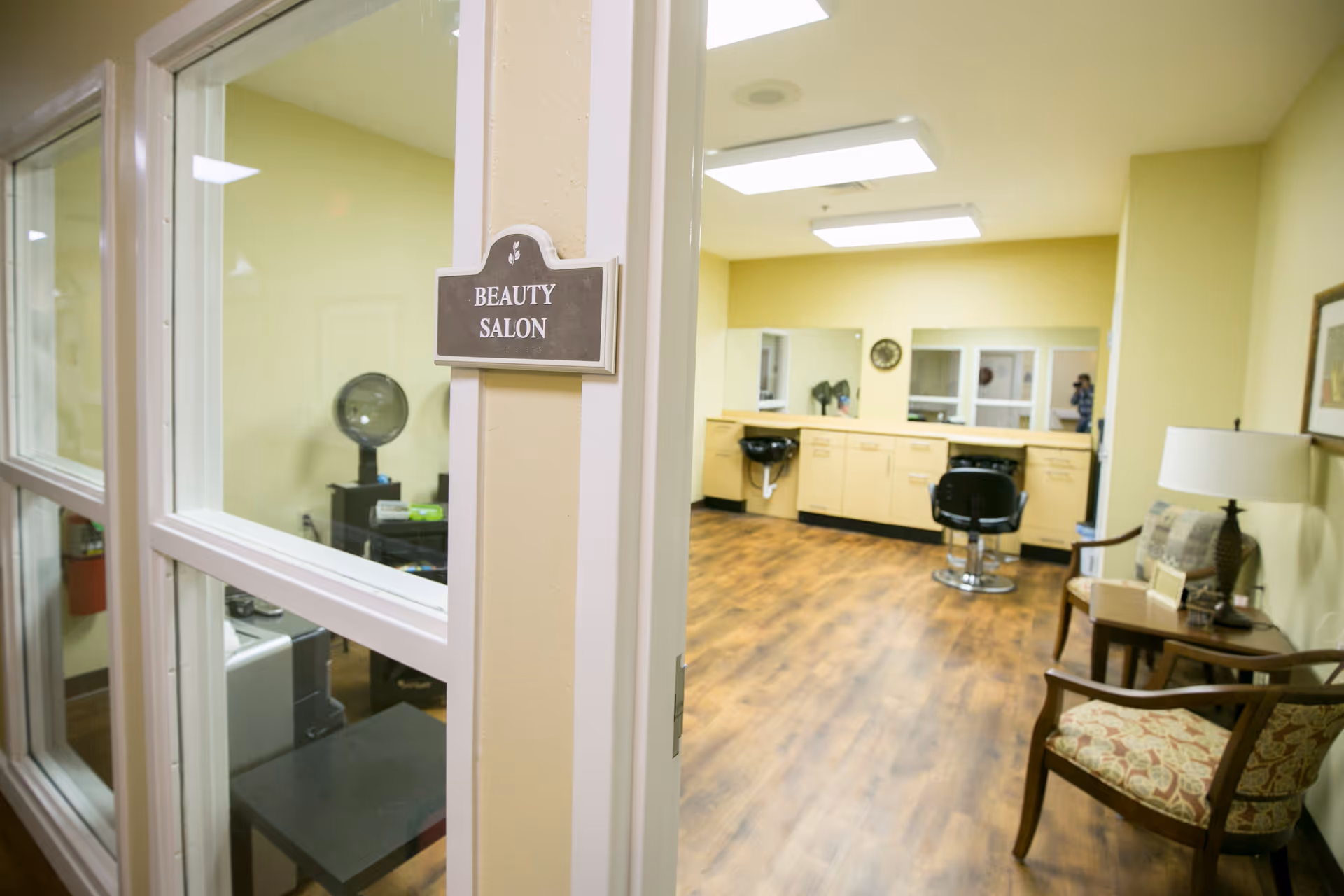 View into a beauty salon showing a 'Beauty Salon' sign on the door frame, styling chairs, mirrors, and seating in a well-lit room.