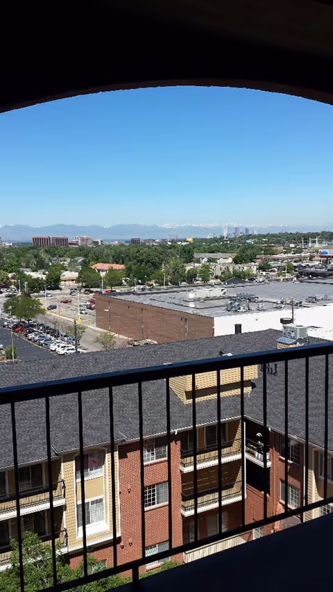 View from a balcony showing a brick building, trees, cityscape, and distant mountains.