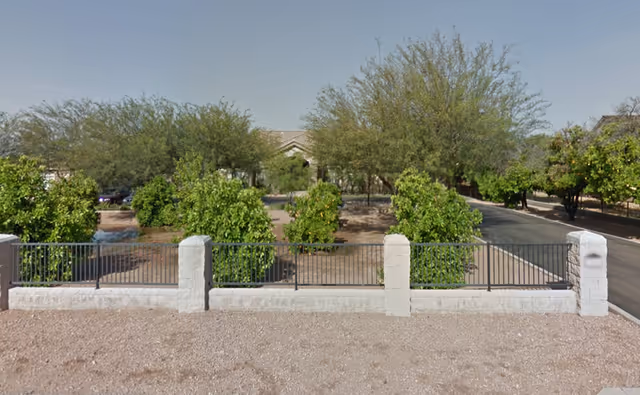 Gated, tree-lined facility exterior with a stone fence and gravel foreground.