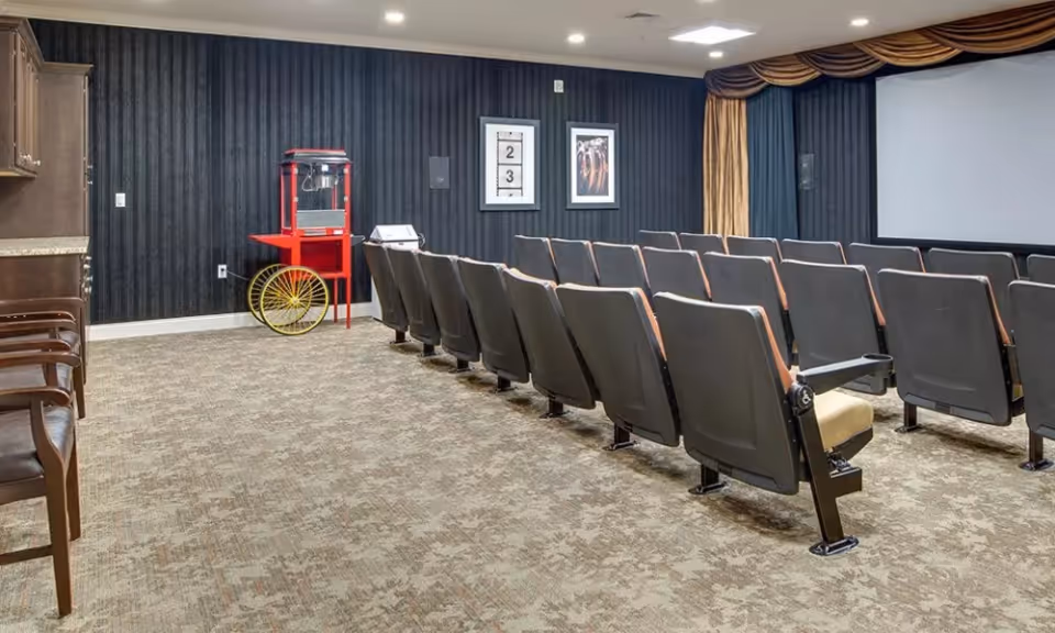 Small movie screening room with rows of auditorium seats facing a projection screen and a popcorn cart against a dark wall.