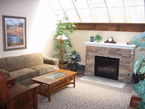 Cozy lounge in a senior living facility with sofa, coffee table, fireplace, and plants.