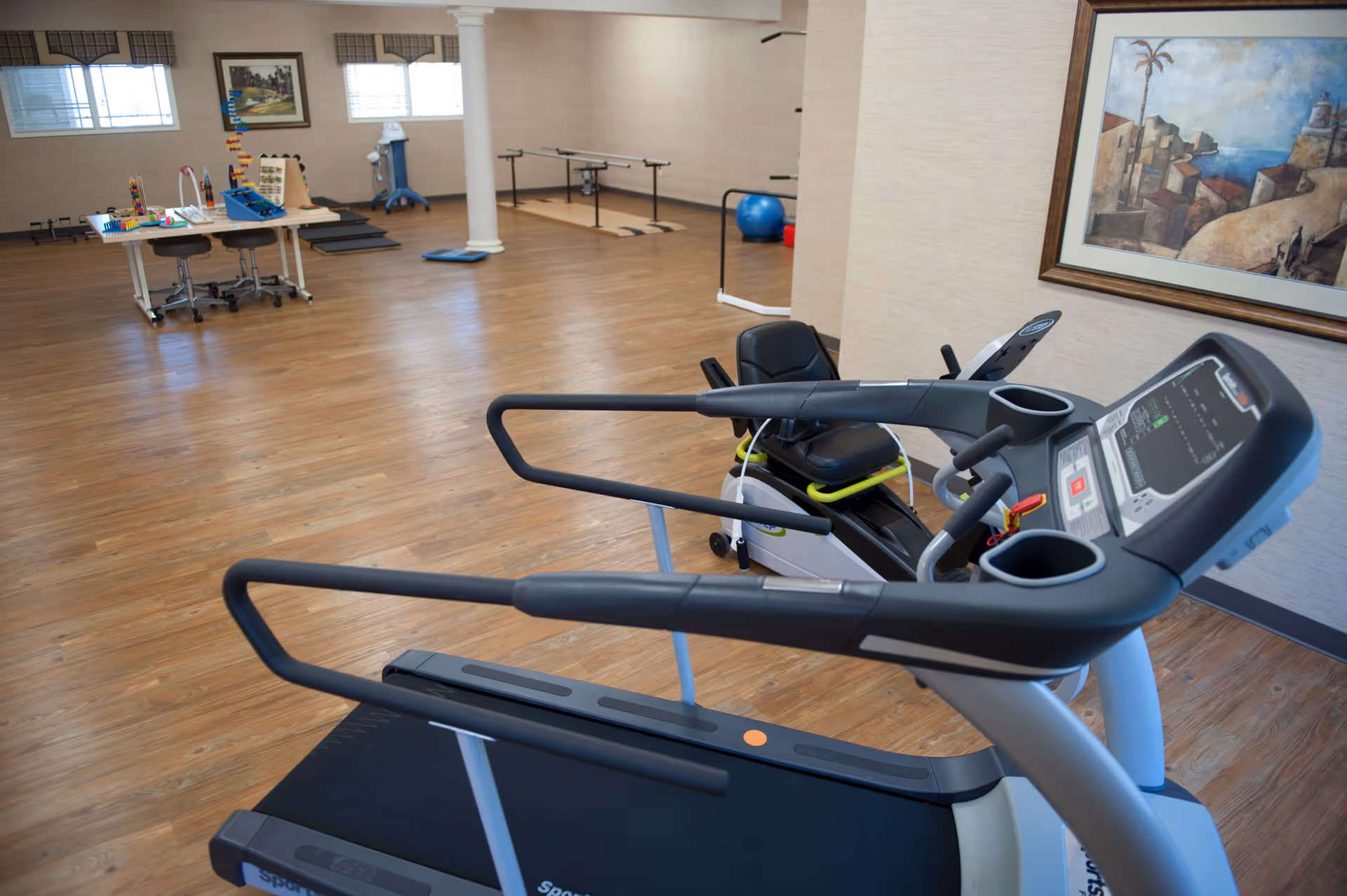 Spacious interior fitness and activity room with treadmills, exercise equipment, and a table with activity toys on a wood floor.