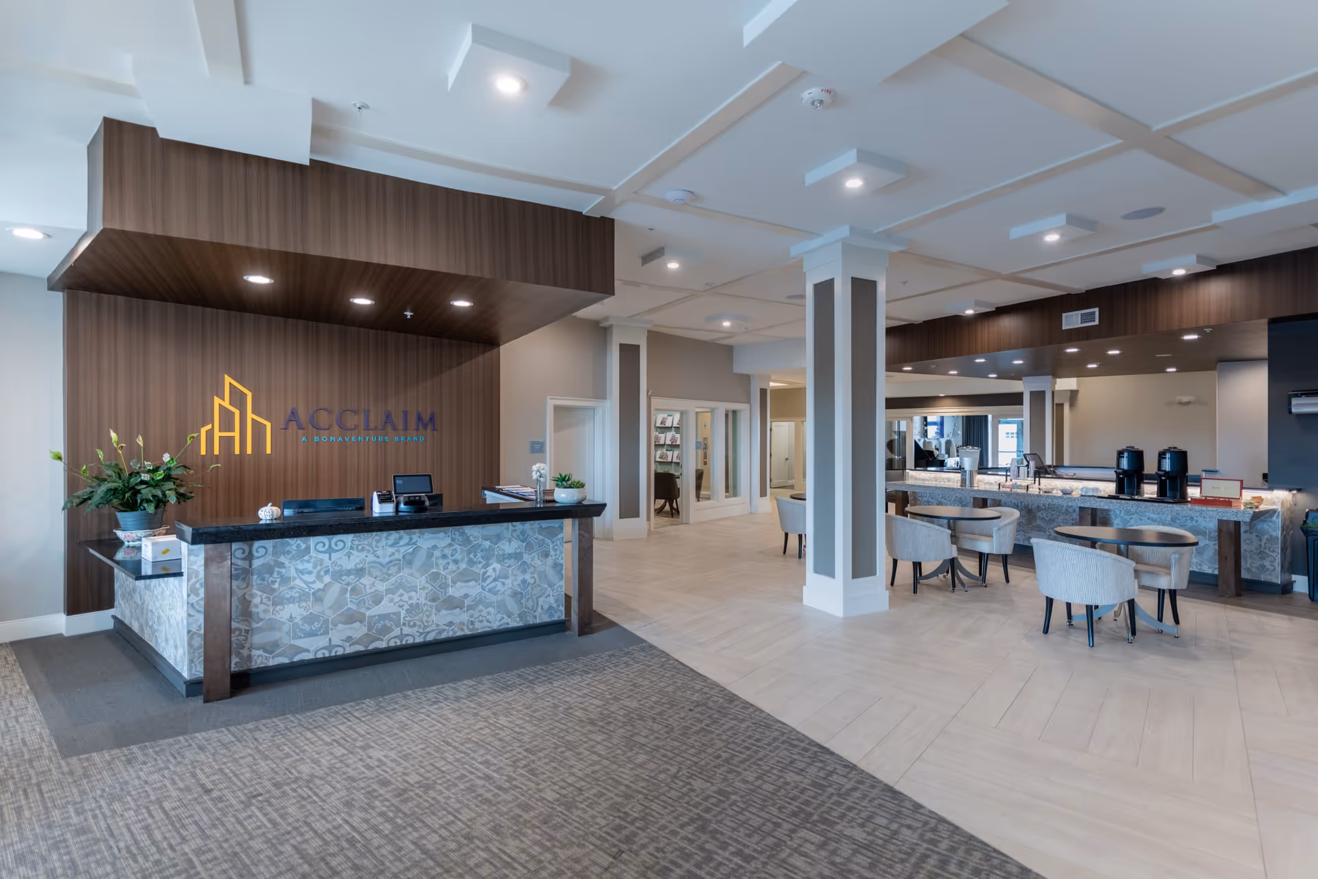 Modern senior living facility lobby with a reception desk, seating area, and 'Acclaim' logo on the wood-paneled wall.