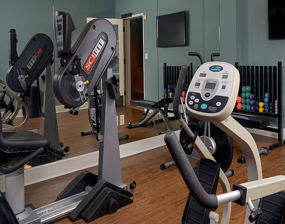 Exercise room with cardio machines, a dumbbell rack and a wall-length mirror.