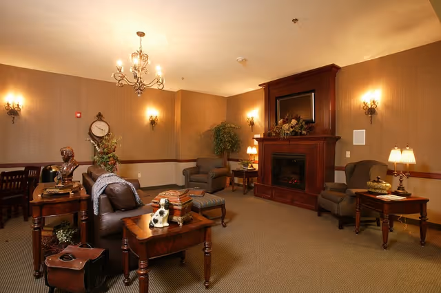 Warmly lit communal living room with a fireplace, armchairs, side tables, and decorative lighting.