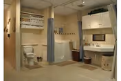 Accessible bathroom with a toilet, walk-in shower with privacy curtains, sink and mirror, and storage cabinets.