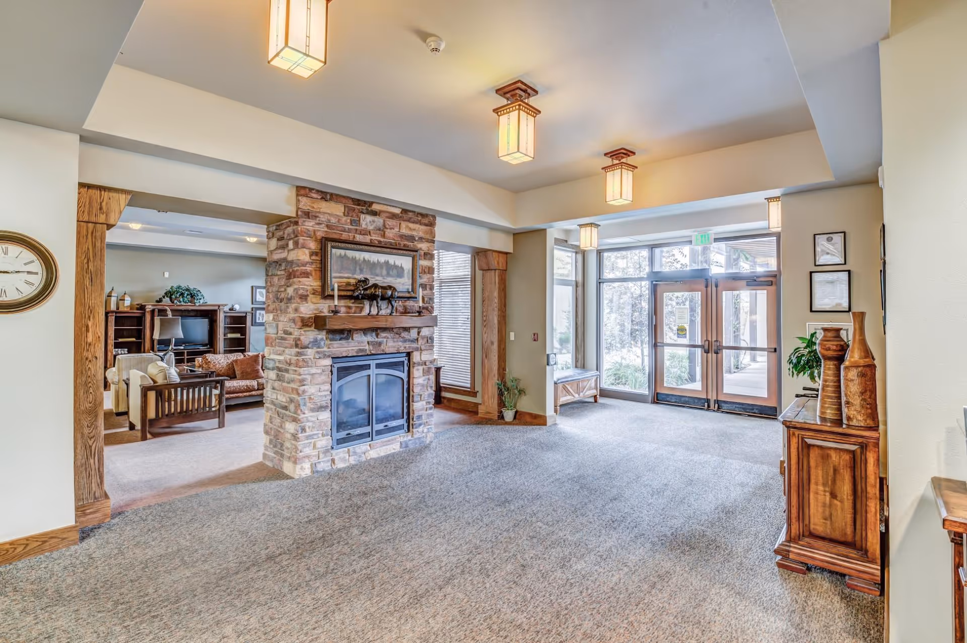 Spacious assisted living lobby with a stone fireplace, seating area, and glass double doors leading outside.