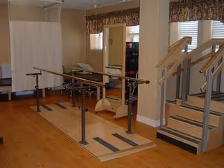 Therapy room with parallel bars, mats, and steps for gait training in a senior living facility.