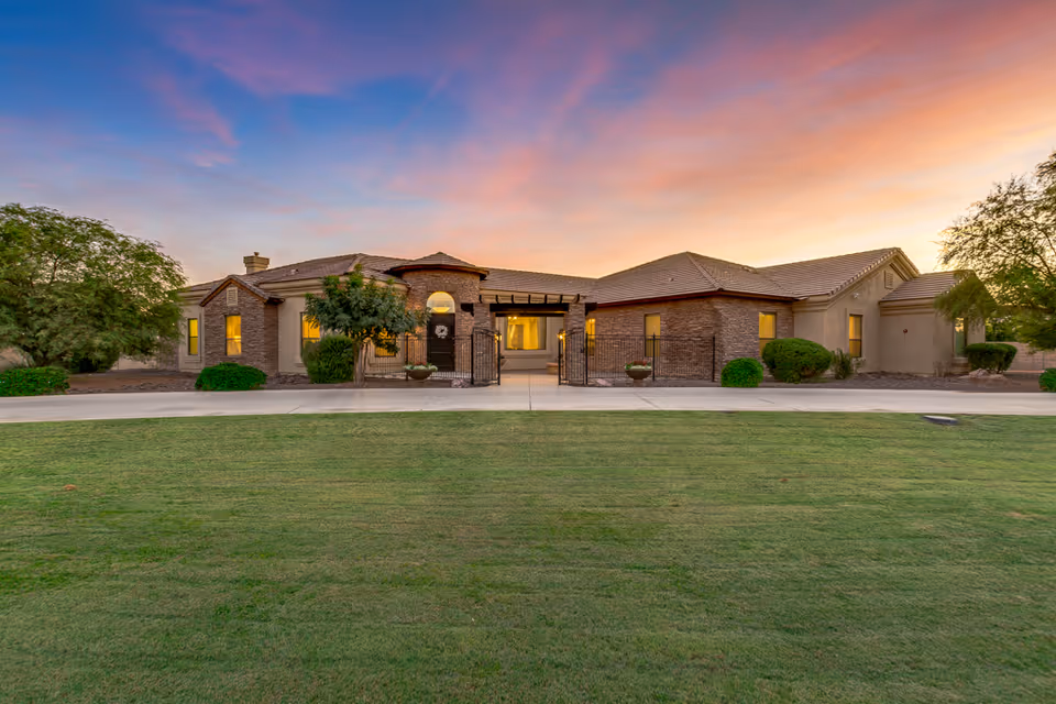 Exterior view of a single-story assisted living facility building at sunset with a well-maintained green lawn in the foreground and trees on either side.