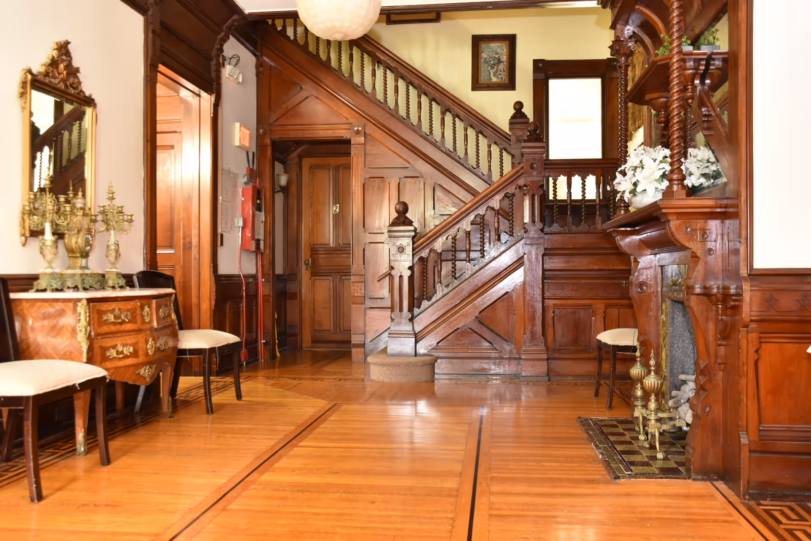 Ornate wooden foyer with a carved staircase, fireplace, and antique furniture.