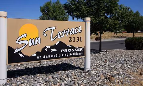 This exterior shows the Sun Terrace Prosser sign with mountains and rocky landscaping.