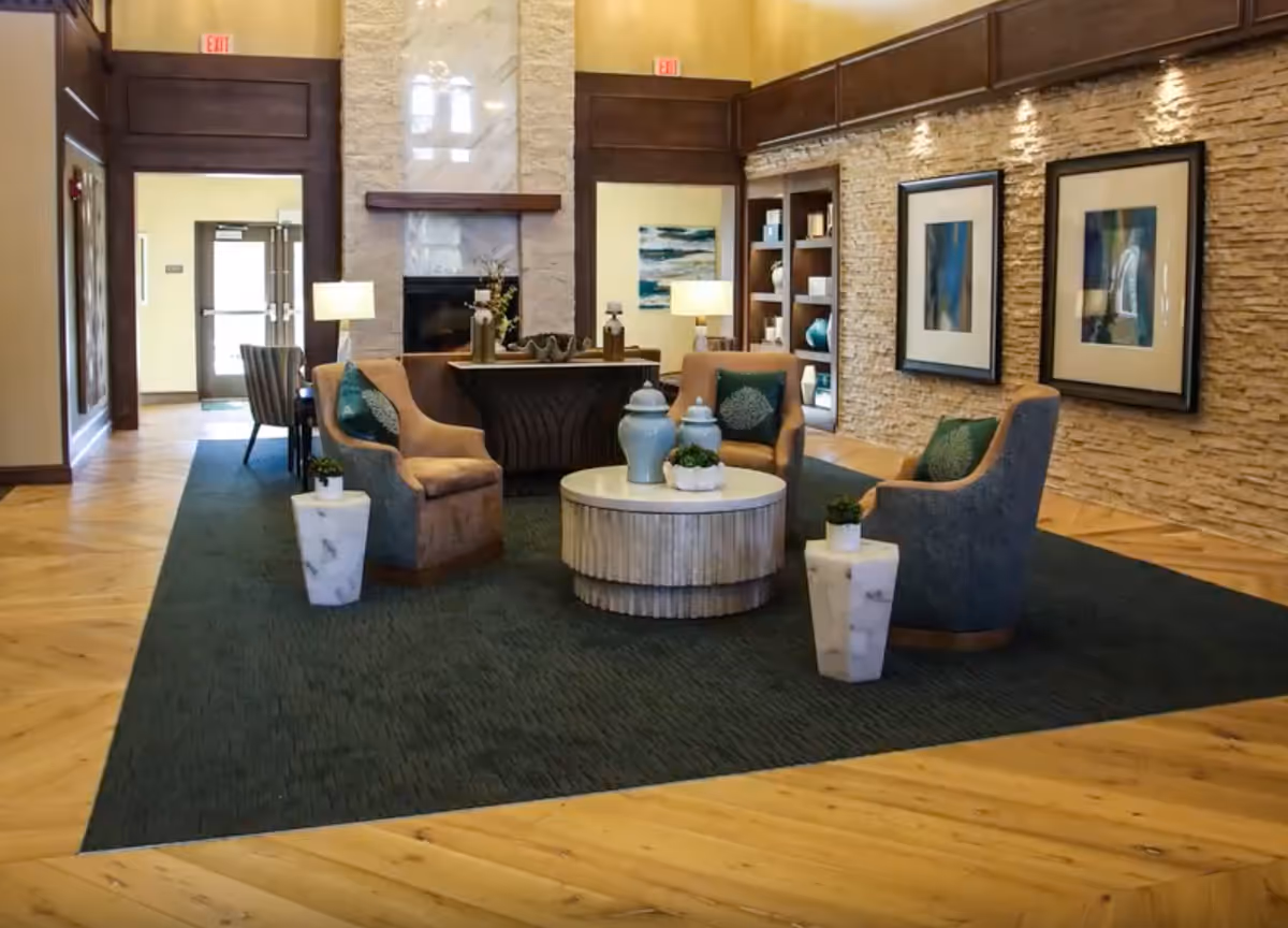 A comfortable lobby seating area with armchairs arranged around a round coffee table, a fireplace, and a stone-accent wall with framed artwork.