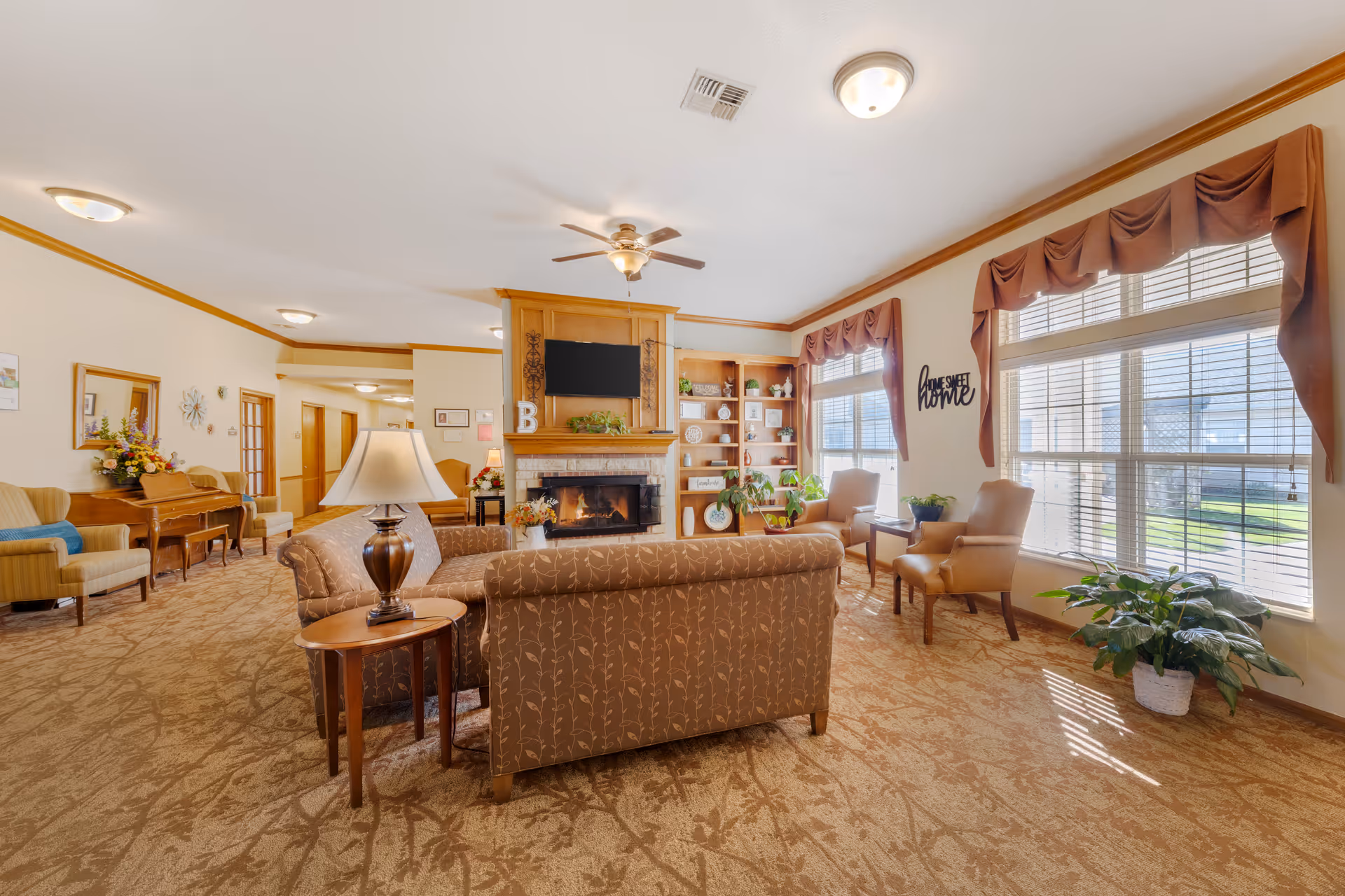 A bright senior living common room with sofas, armchairs, a fireplace and large windows letting in natural light.