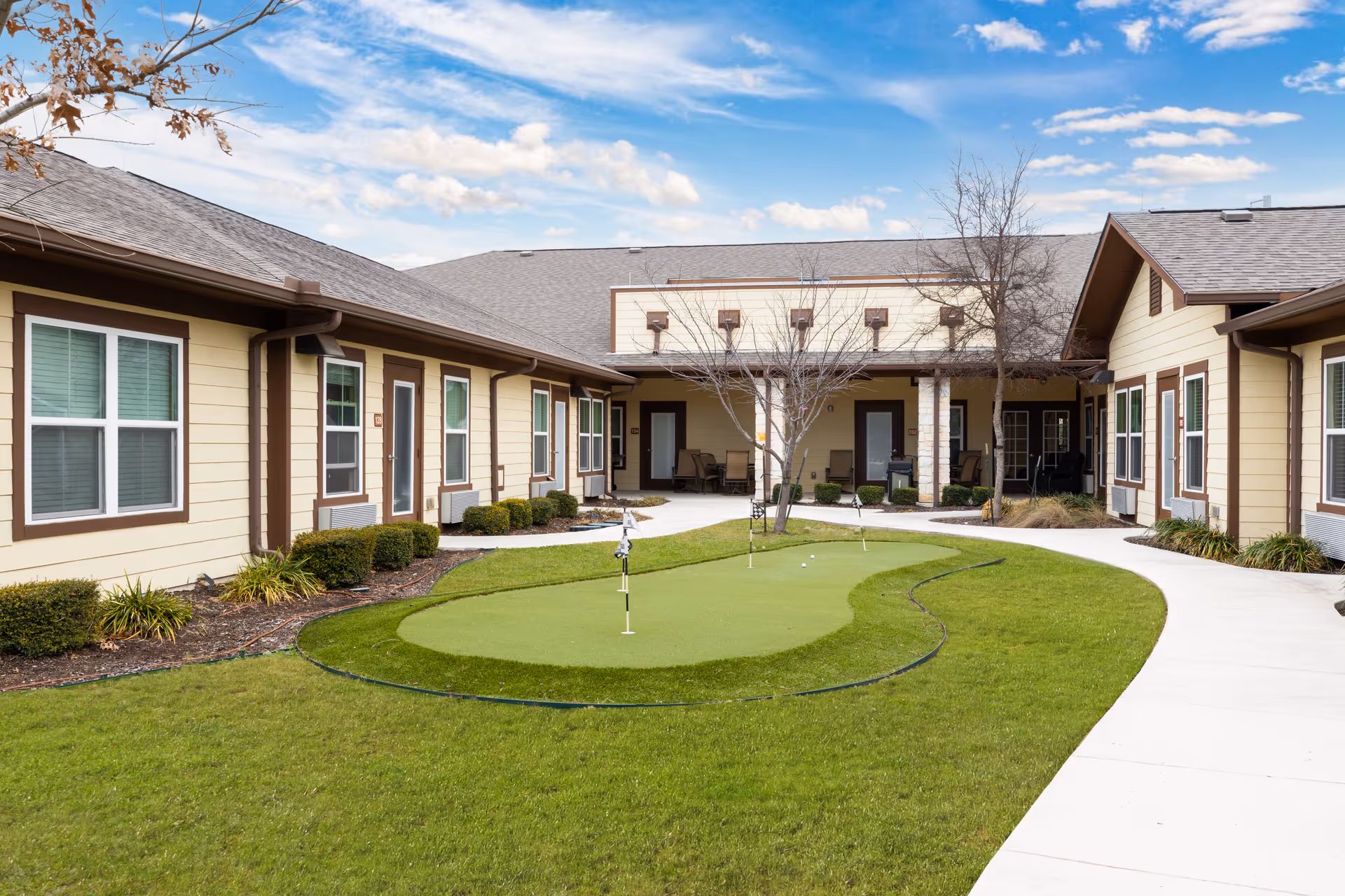 Outdoor courtyard with a small putting green, pathways, and single-story beige buildings surrounding it.