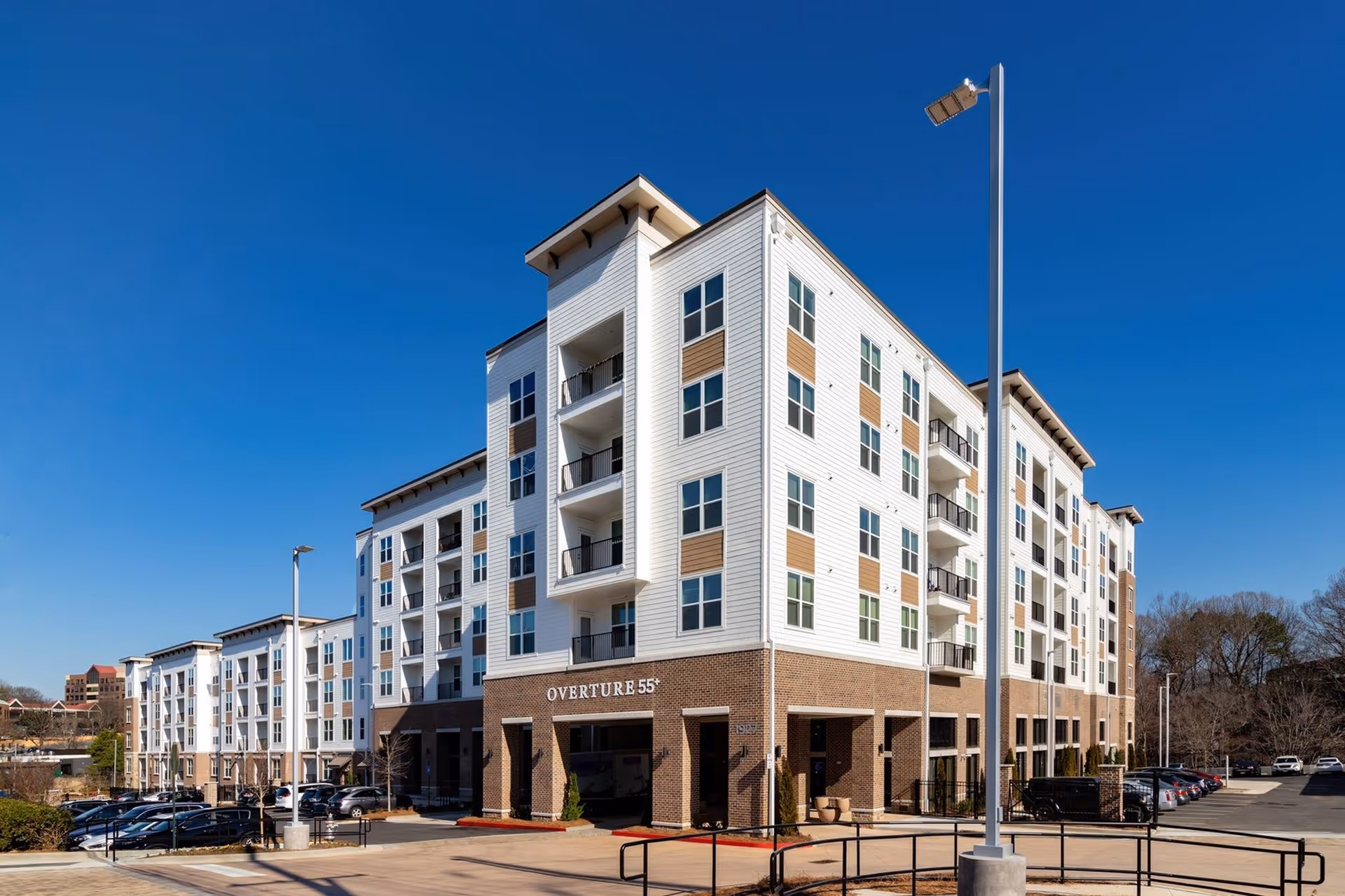 Exterior view of a modern multi-story residential building named Overture 55+, with a clear blue sky and a parking lot in front.