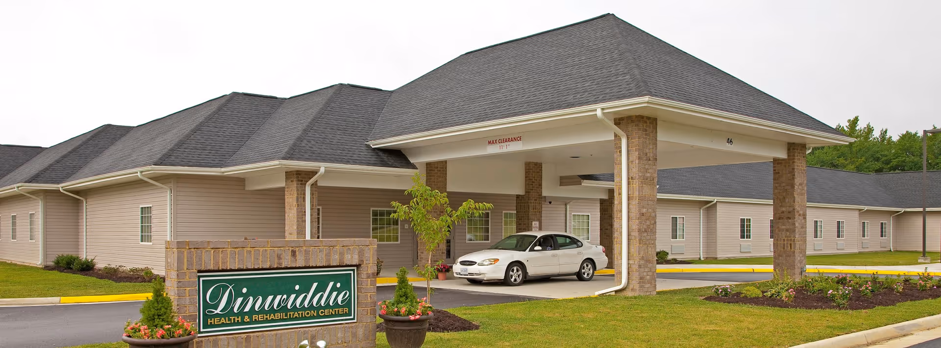 Front exterior of Dinwiddie Health & Rehabilitation Center with a covered porte-cochere, parked car, entrance drive, sign, and landscaping.