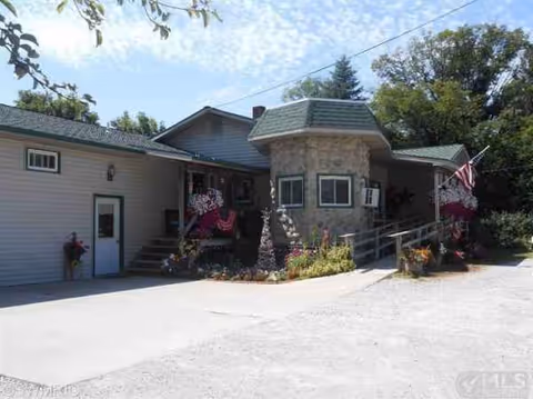 Front exterior of a small facility with stone accents, porch seating, flowers, and an American flag.