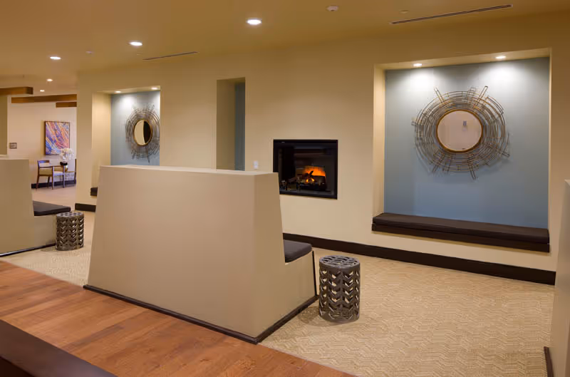 Modern communal lounge with a built-in fireplace, bench seating in recessed niches, decorative circular mirrors, and small side tables.