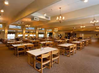 A spacious dining room with numerous wooden tables, chairs, and warm ceiling lighting.
