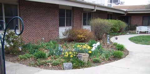 Brick exterior of Spurgeon Manor with curved walkway, flower beds, and a white bench.