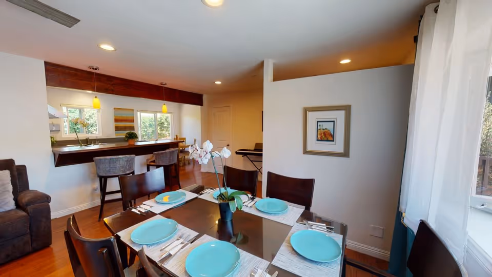 A dining table set with turquoise plates in an open-plan dining area overlooking a kitchen and living room.